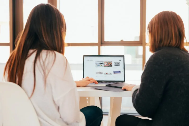 Two women in conversation viewing a laptop screen together